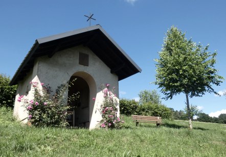 Kleine Kapelle im Grünen, umgeben von blühenden Rosen. Eine Bank steht daneben, ein Baum spendet Schatten. Blauer Himmel im Hintergrund., © Tourist-Information Bitburger Land, Melanie Salzburger Kleine Kapelle im Grünen, umgeben von blühenden Rosen. Eine Bank steht daneben, ein Baum spendet Schatten. Blauer Himmel im Hintergrund., © Tourist-Information Bitburger Land, Melanie Salzburger