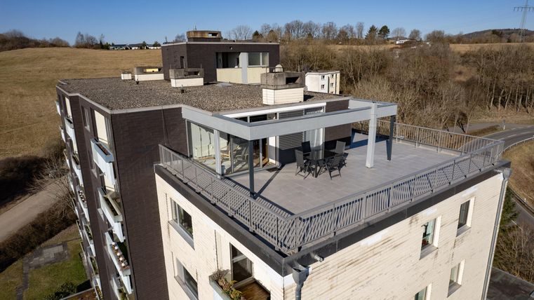 Een modern appartementencomplex met een ruime balkon. Op de achtergrond zijn zachte heuvels en een heldere lucht te zien.