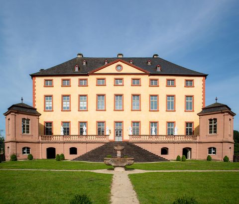 Un château historique avec une façade élégante et de grandes fenêtres. Il est situé dans un environnement verdoyant avec un jardin bien entretenu.