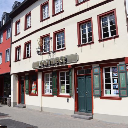 Un bâtiment historique avec l'inscription "Pharmacie". La façade est peinte en clair et a de nombreuses fenêtres avec des jardinières.