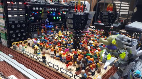 A lively scene featuring many LEGO figures at a concert. In the background, you can see a stage with colorful lights and a large crowd.