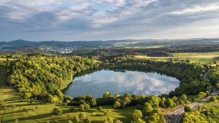 Een pittoresk meer omringd door weelderig groen en zachte heuvels. De lucht is wisselvallig met wolken en een heldere blauwe lucht.