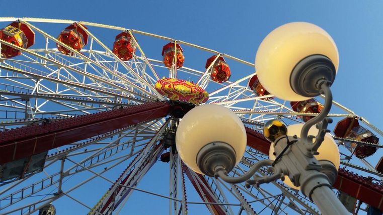 Ein großes Riesenrad vor einem klaren blauen Himmel. Im Vordergrund sind Straßenlampen sichtbar.