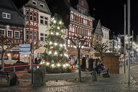 Un sapin de Noël joliment décoré se dresse dans une ville enneigée. Les lumières et les cadeaux rouges confèrent une ambiance chaleureuse à la scène.