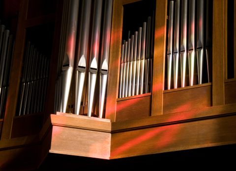 Eine Orgel mit glänzenden Metallpfeifen und warmem Holz. Sanftes Licht fällt auf die Oberfläche und erzeugt schöne Farben.