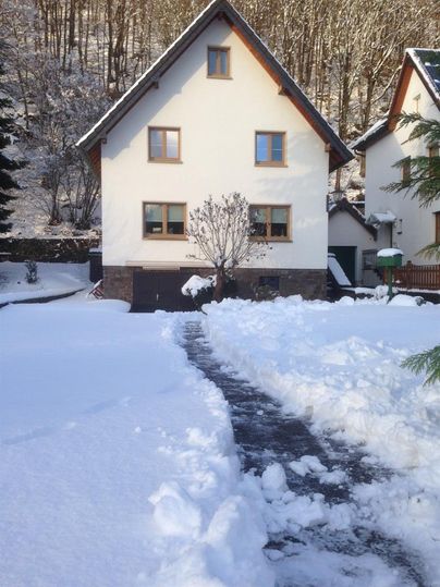 A winter house with a snow-covered garden. The path to the entrance is cleared, and the trees are covered in snow.