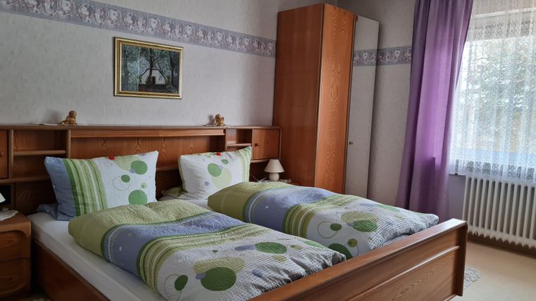 Ein gemütliches Schlafzimmer mit einem Doppelbett und bunten Bettdecken. Die Wände sind hell, und große Fenster lassen viel Tageslicht herein.