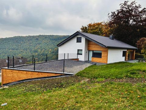 Ein modernes Haus mit einer Kombination aus Holz- und Putzfassade. Es liegt in einer grünen Umgebung mit sanften Hügeln im Hintergrund.