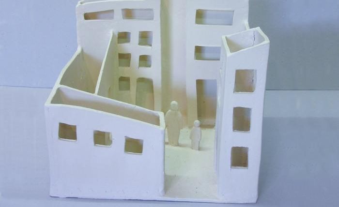 A model of an urban space with white walls and several windows. Two figures stand in the center of the model.
