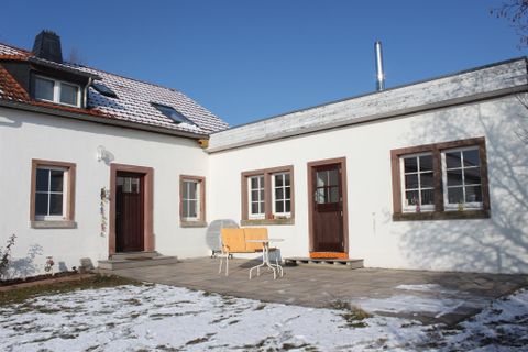 Ein modernes Haus mit einem gepflasterten Patio. Der Bereich ist teilweise mit Schnee bedeckt und es gibt Stühle im Freien.