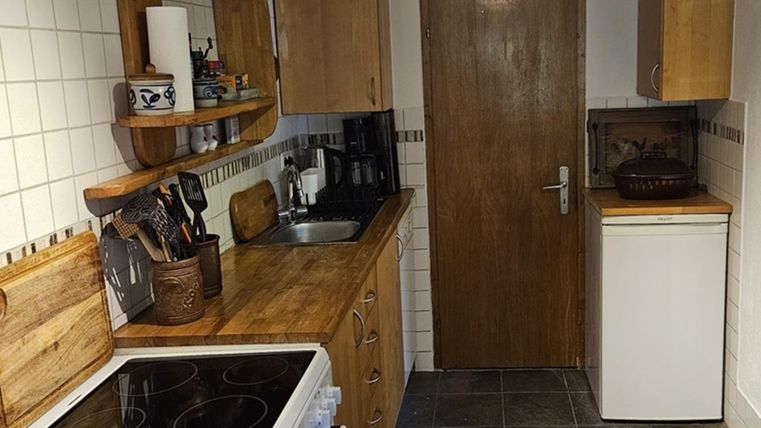 Een gezellige keuken met houtenkasten en moderne apparaten. De wanden zijn betegeld, en er is een koelkast naast een deur.