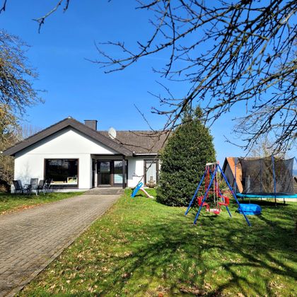 Ein modernes Einfamilienhaus mit einem schönen Garten und einem Spielplatz. Der Himmel ist klar und blau, ideal für Familienaktivitäten im Freien.