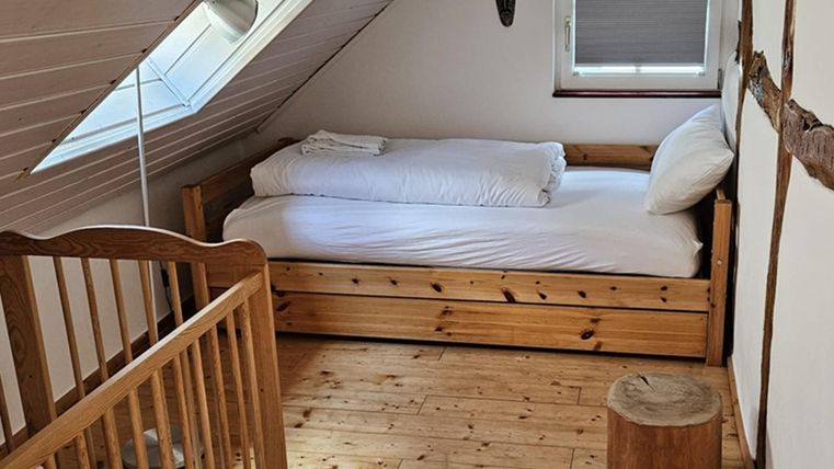 Een gezellige slaapkamer met een eenpersoonsbed en een kinderbed. De ruimte heeft een houten vloer en een heldere, uitnodigende sfeer.