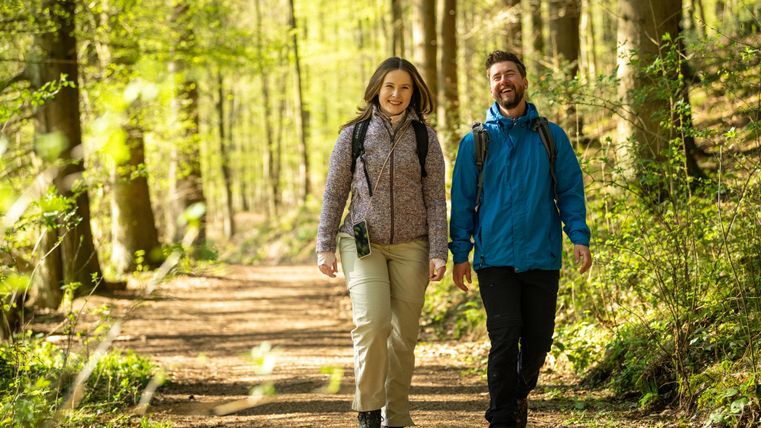 A couple is hiking on a forest path and enjoying nature. Surrounded by green trees, they radiate joy and relaxation.