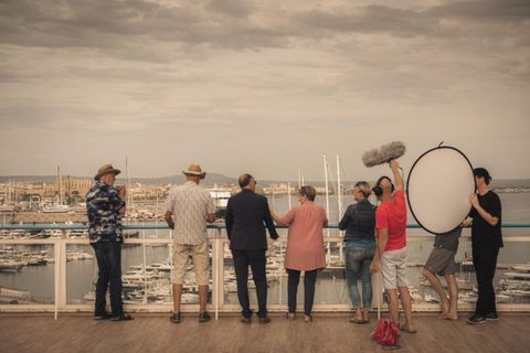 5 amateur actors with 3 film technicians at a railing overlooking a marina.