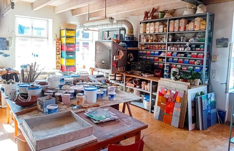 Ein kreatives Atelier mit vielen Werkzeugen und Materialien. Tische sind mit Farbbehältern und Kunstwerken gefüllt.