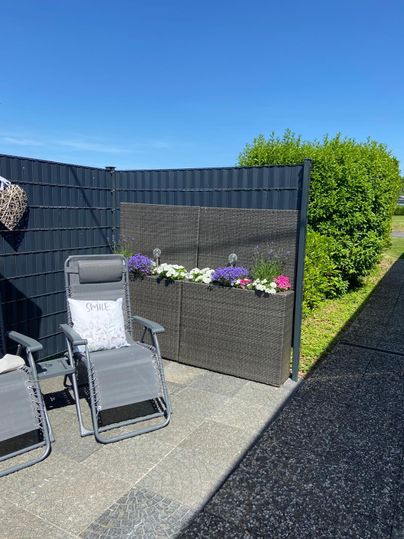 A peaceful outdoor area with two lounge chairs and colorful flowers in a flower box. The sky is clear and blue, surrounded by green grass.