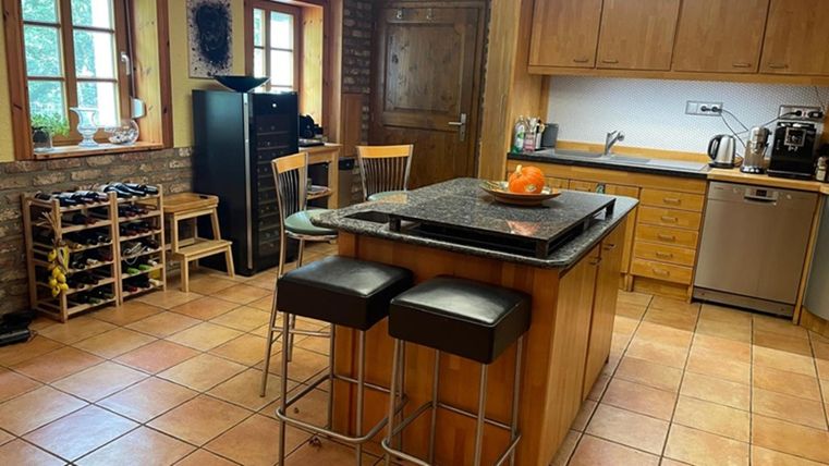 A modern kitchen with a central island and bar stools. It is bright and well-equipped, with wood and stone aesthetics.