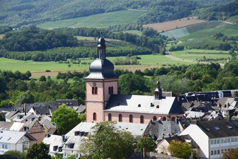 Une ville pittoresque avec une église et des collines verdoyantes en arrière-plan. Les toits des maisons sont variés et la nature est luxuriante.