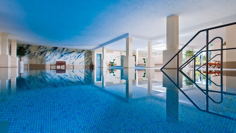 Een elegante binnenzwembad met blauw water en moderne pilaren. Aan de rand is er een trap en enkele planten op de achtergrond.