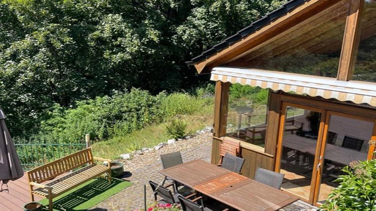 A cozy wooden house with a terrace and an outdoor dining table. Surrounded by plenty of greenery and trees, it offers a quiet retreat.