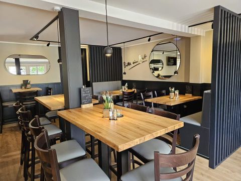 Ein modernes Restaurant mit Holztischen und Stühlen. Die Wände sind in neutralen Farben gehalten und spiegeln eine einladende Atmosphäre wider.