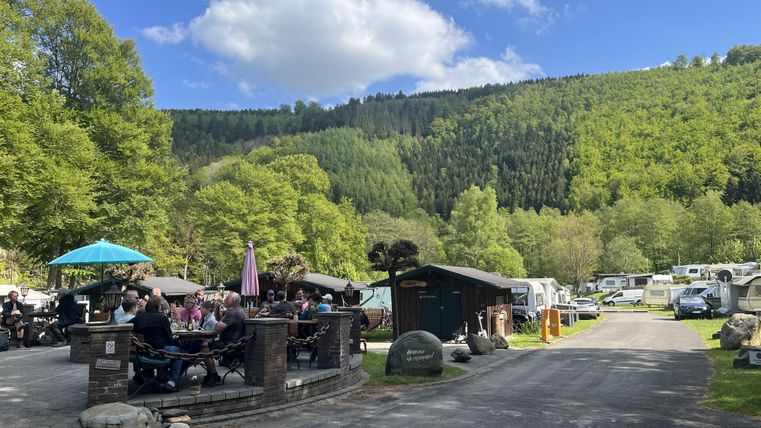 Un camping dans un environnement idyllique avec des collines verdoyantes. Plusieurs camping-cars sont sur le site, et un groupe de personnes est assis confortablement à l'extérieur.
