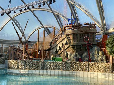 Ein aufregendes Spielschiff in einem Wasserpark, umgeben von Felsen und Pflanzen. Es ist in einer großen, lichtdurchfluteten Halle untergebracht.