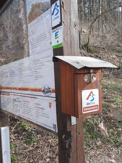 Een informatiestand met een houten kist en een kaartbord. De omgeving is natuurlijk en groen.