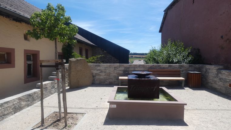 Een rustplaats in Trimport met een fontein, een bankje en een boom.