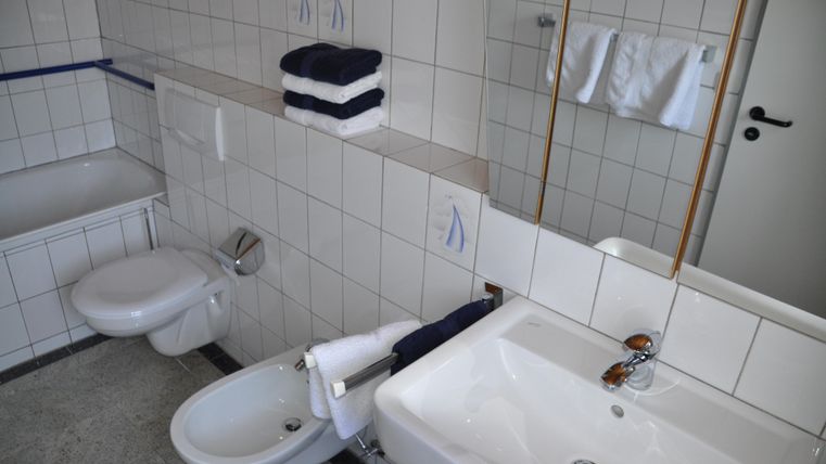 A modern bathroom with white tiles. Towels and toiletries are neatly arranged.