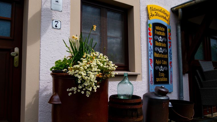 A charming house with a window and a colorful sign. In front of the door, there is a flower pot with blooming plants.