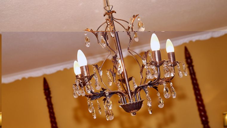 Eine elegante Deckenlampe mit Kristallanhängern und mehreren Leuchten. Sie hängt in einem Zimmer mit gelben Wänden.