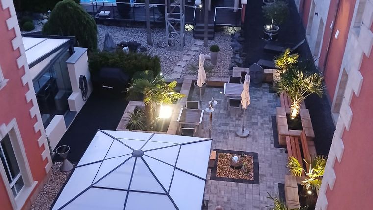 Ein schöner Innenhof mit einer Pergola und komfortablen Sitzgelegenheiten. Im Hintergrund sind Bäume und ein Pool sichtbar.