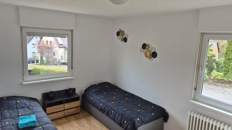 Een helder slaapkamer met twee eenpersoonsbedden en een eenvoudige nachtkastje. Grote ramen bieden uitzicht naar buiten en zorgen voor veel licht.