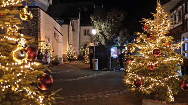 Ein festlich geschmückter Platz mit beleuchteten Weihnachtsbäumen. Die Atmosphäre ist gemütlich und weihnachtlich.