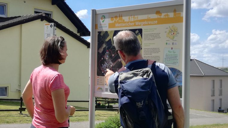 Two people are looking at a hiking board outdoors.