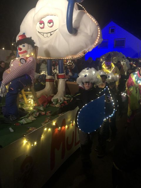 Ein nächtlicher Umzug mit bunten Figuren und festlicher Beleuchtung. Kinder tragen kreative Kostüme und es herrscht eine fröhliche Atmosphäre.