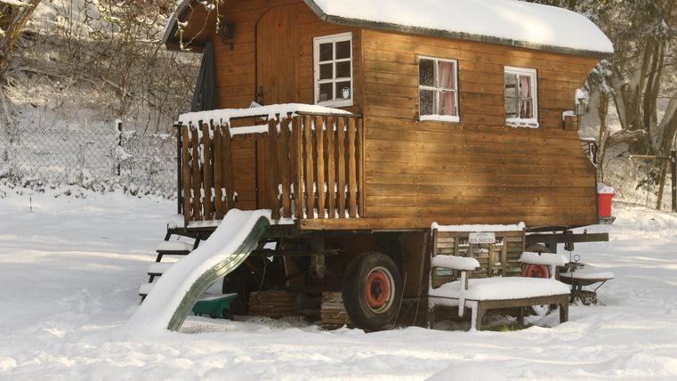 Eine gemütliche Holzhütte steht in einer schneebedeckten Landschaft. Vor der Hütte gibt es eine kleine Treppe und eine Rutsche.