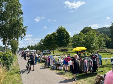 Un marché aux puces au bord de la route avec des stands proposant des vêtements et d'autres marchandises. Les gens flânent et profitent du beau temps.