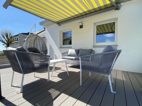 Un espace extérieur confortable avec deux fauteuils modernes et une table. Au-dessus de la zone, un parasol rayé est déployé et en arrière-plan, un fauteuil suspendu est visible.