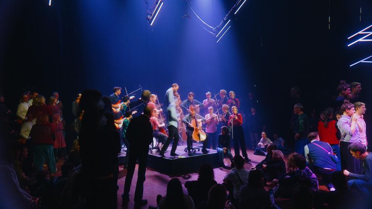 A lively event with musicians on a stage and an engaged crowd. Colorful lights and a cheerful atmosphere create an inviting vibe.