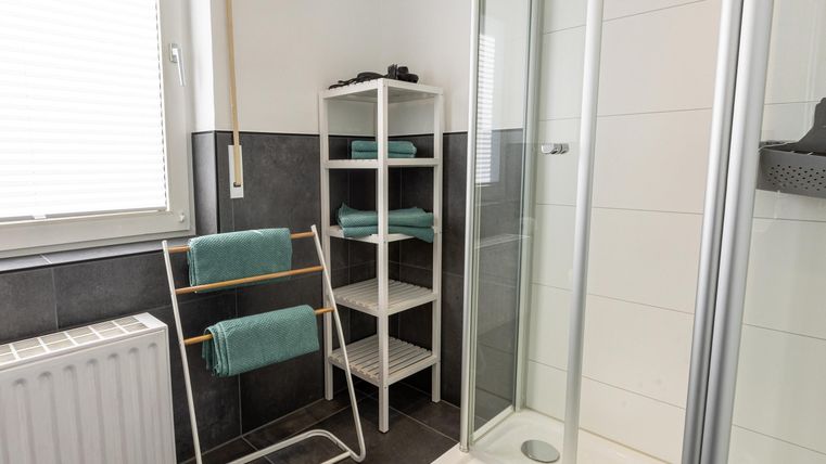 Een moderne badkamer met een douche en een rek voor handdoeken. De muren zijn in neutrale kleuren gehouden en er is veel daglicht.