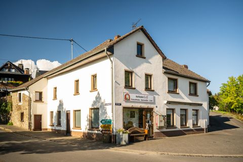 Un bâtiment charmant et blanc au bord d'une rue. Il s'agit d'une auberge avec une entrée accueillante et entourée d'arbres.