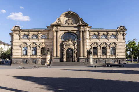Een hand houdt een gebogen vel papier vast. De achtergrond bevat informatie over een tentoonstelling in het Leopold-Hoesch-Museum.