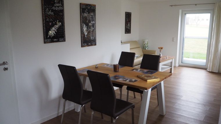 Ein modernes Esszimmer mit einem Tisch und vier Stühlen. Große Fenster sorgen für lichtdurchflutete Atmosphäre.