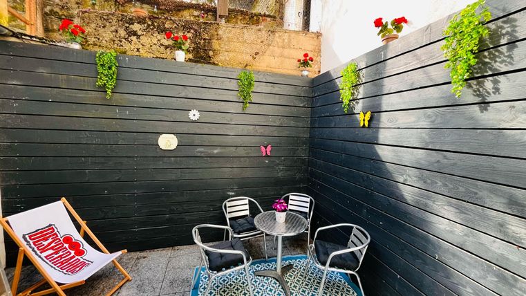 Een gezellige binnenplaats met zwarte wandbekleding en groene planten. Twee stoelen en een tafel staan klaar om te genieten van de ontspannen sfeer.