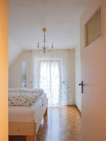 Une chambre confortable avec un grand lit et des rideaux floraux. La pièce a une vue lumineuse et accueillante sur la lumière du jour.