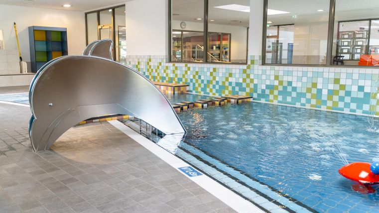 Une piscine intérieure moderne avec un toboggan et des carreaux colorés. L'eau est claire et la zone est bien éclairée.