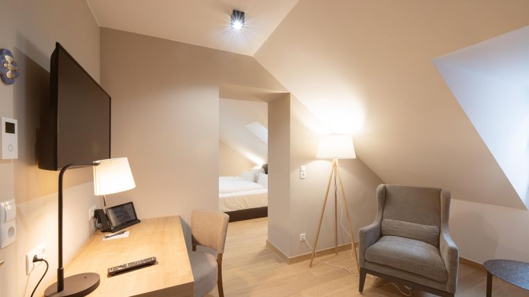 Een moderne kamer met een tv, een bureau en een comfortabele stoel. De muren zijn licht en de vloer is van hout.